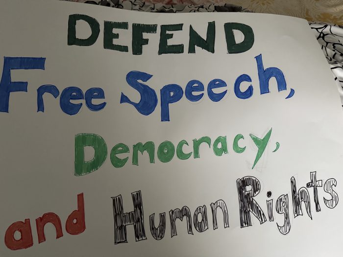 Protest sign reading: Defend Free Speech, Democracy, and Human Rights